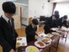 舎生が机に並んでいる食事を皿に取っているところ