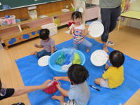 紙粘土の入ったたらいを囲む幼児たち。紙皿に紙皿にマジックで絵を描いている。