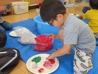 幼児が紙皿に紙粘土を貼り付けている。