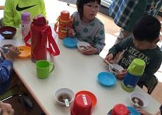 テーブルにぜんざいの入ったお椀と水筒とお皿。２人の幼児が食べている。