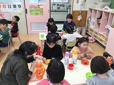３つのテーブルに分かれて座った子どもたち。お皿に入った菜っ葉を食べる。