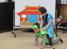 劇「うらしまたろう」　竜宮城の絵の前で亀役の子が四つ葉胃になり、浦島太郎役の子がまたがっている。