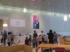 美術館受付前で美術館の人が話をする。幼児は横一列に並んで聞いている。その後ろに教員数名。