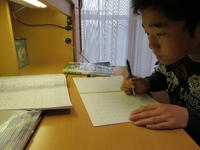 教科書をのぞき込み，漢字の書き取りをしているところ