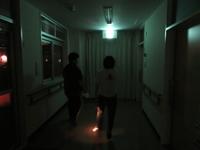 真っ暗な中，舎生が懐中電灯を持って廊下を歩いて避難経路を確認しています。